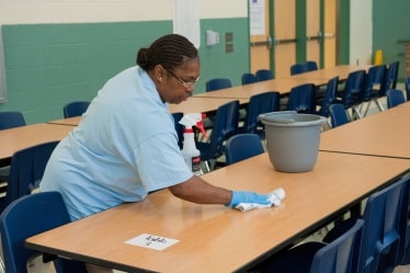 Woman cleaning tables in a school cafeteria.