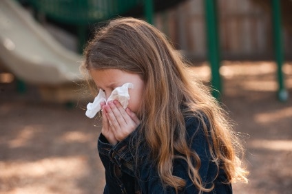 Young girl blowing her nose with a tissue.