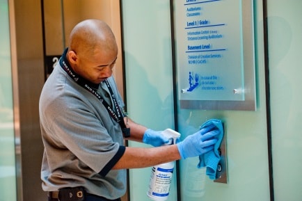 Man cleaning an elevator button in an office building.