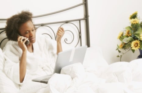 Woman at home in bed working on a computer.