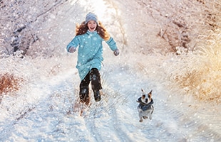 Woman running on snow trail with small dog