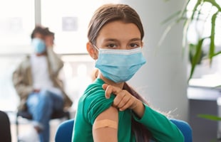 woman showing injection bandaid in green shirt and mask