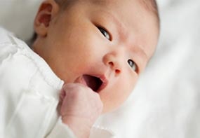 An infant turning her head to the side and putting her hand near her mouth.