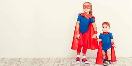 A young girl and her toddler brother in superhero outfits.