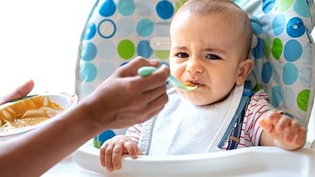 Child in high chair being fed by an adult.