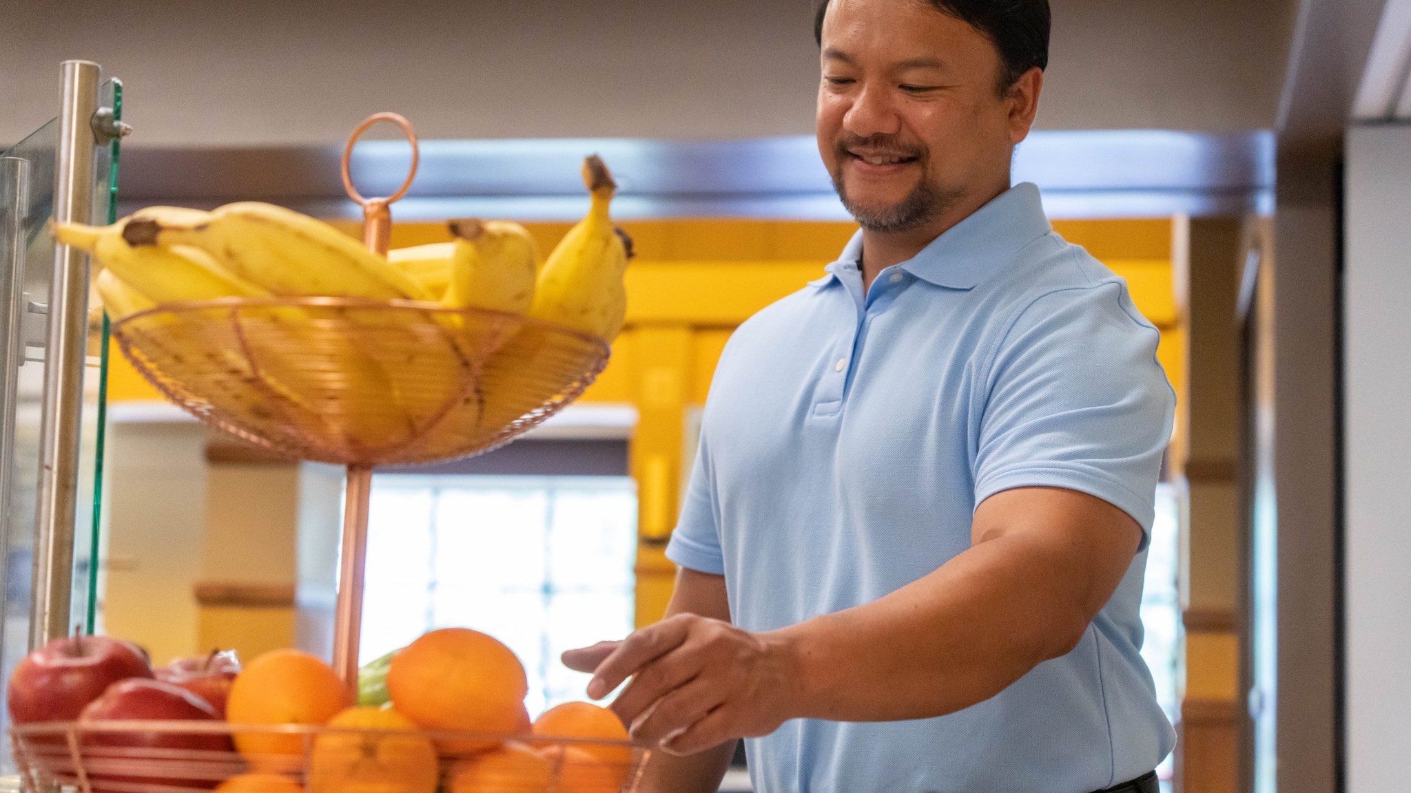 Man reaches for an orange in a display of bananas, apples, and oranges.