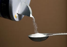 A close up of salt being poured from the container into a measuring spoon.