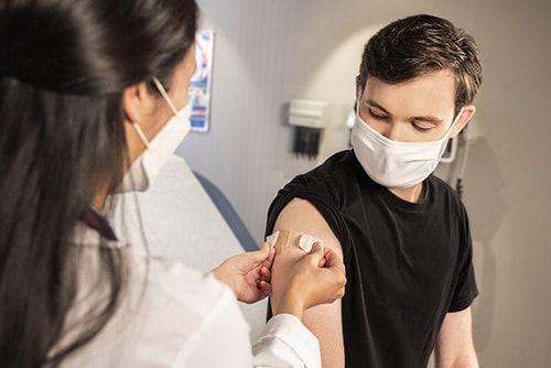 A healthcare practitioner putting a band aid on a young person's arm.
