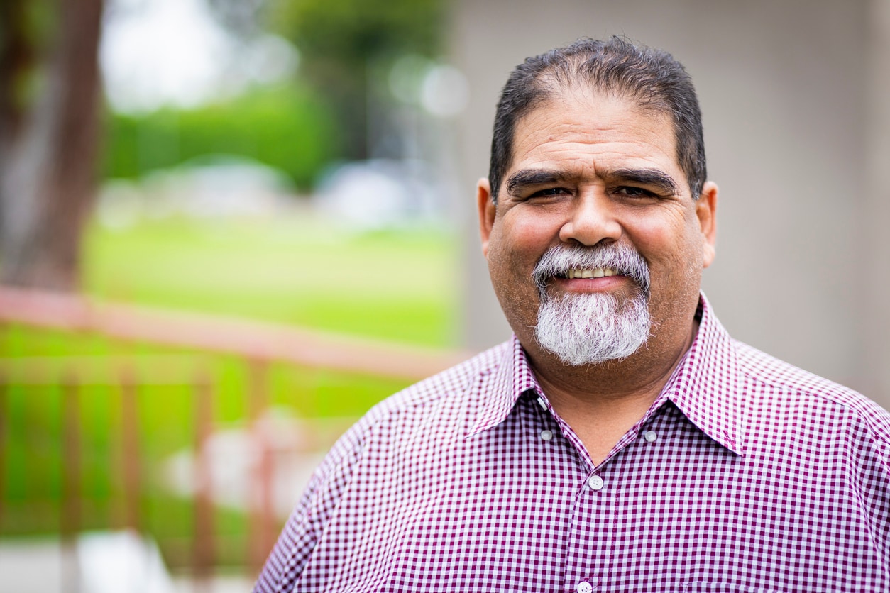 Portrait of an older, Hispanic man wearing a purple button-down shirt.