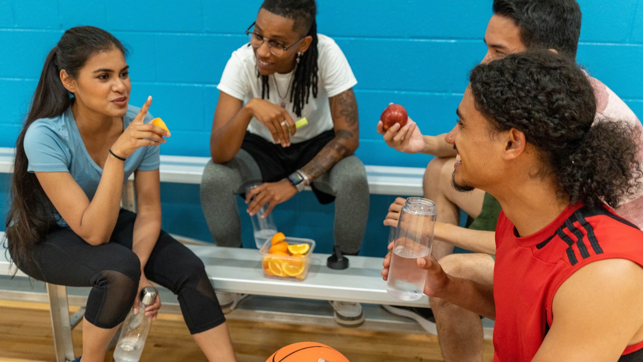 Four young people eating healthy snacks while taking a break from playing basketball.