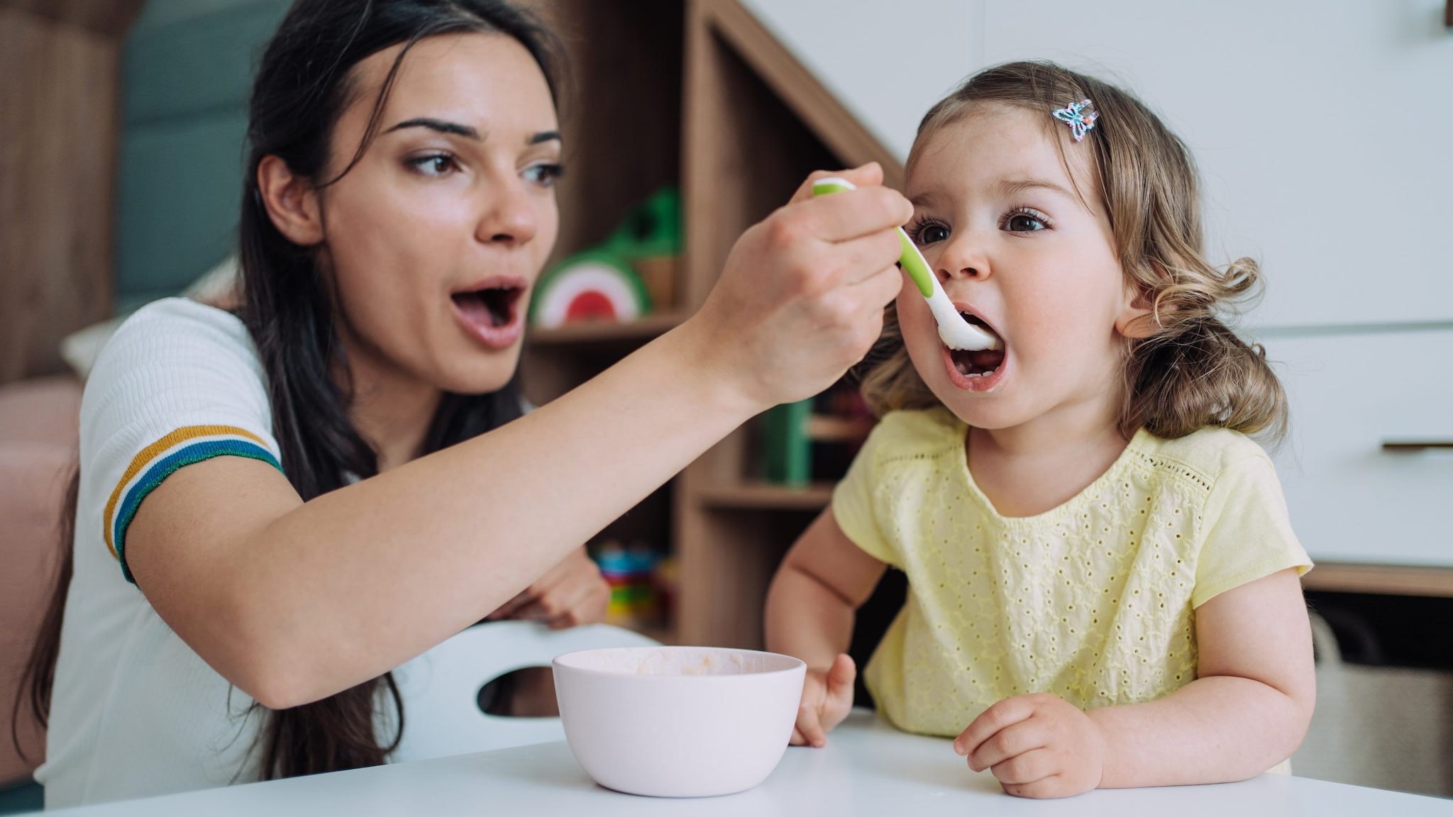 Photo of a woman feeding a young child with a spoon.
