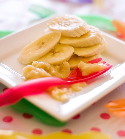 Mashed banana slices on a white plate with a red, plastic fork