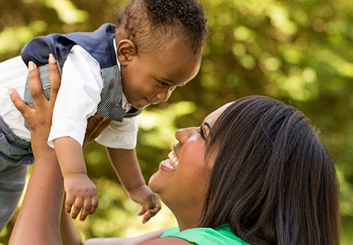 Happy African American female lifting up and smiling at an infant child boy outside