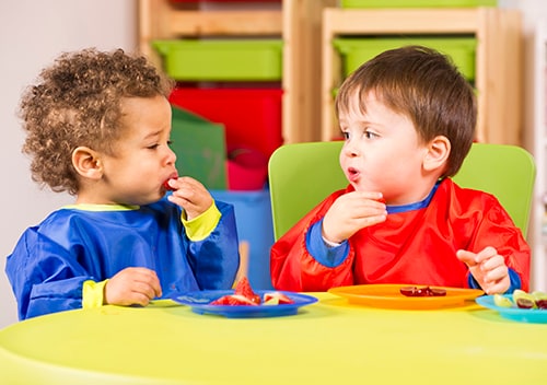 Two young boys eating at a green table in a childcare setting