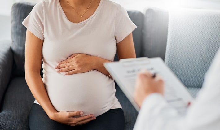 pregnant woman being consulted by doctor holding a clipboard