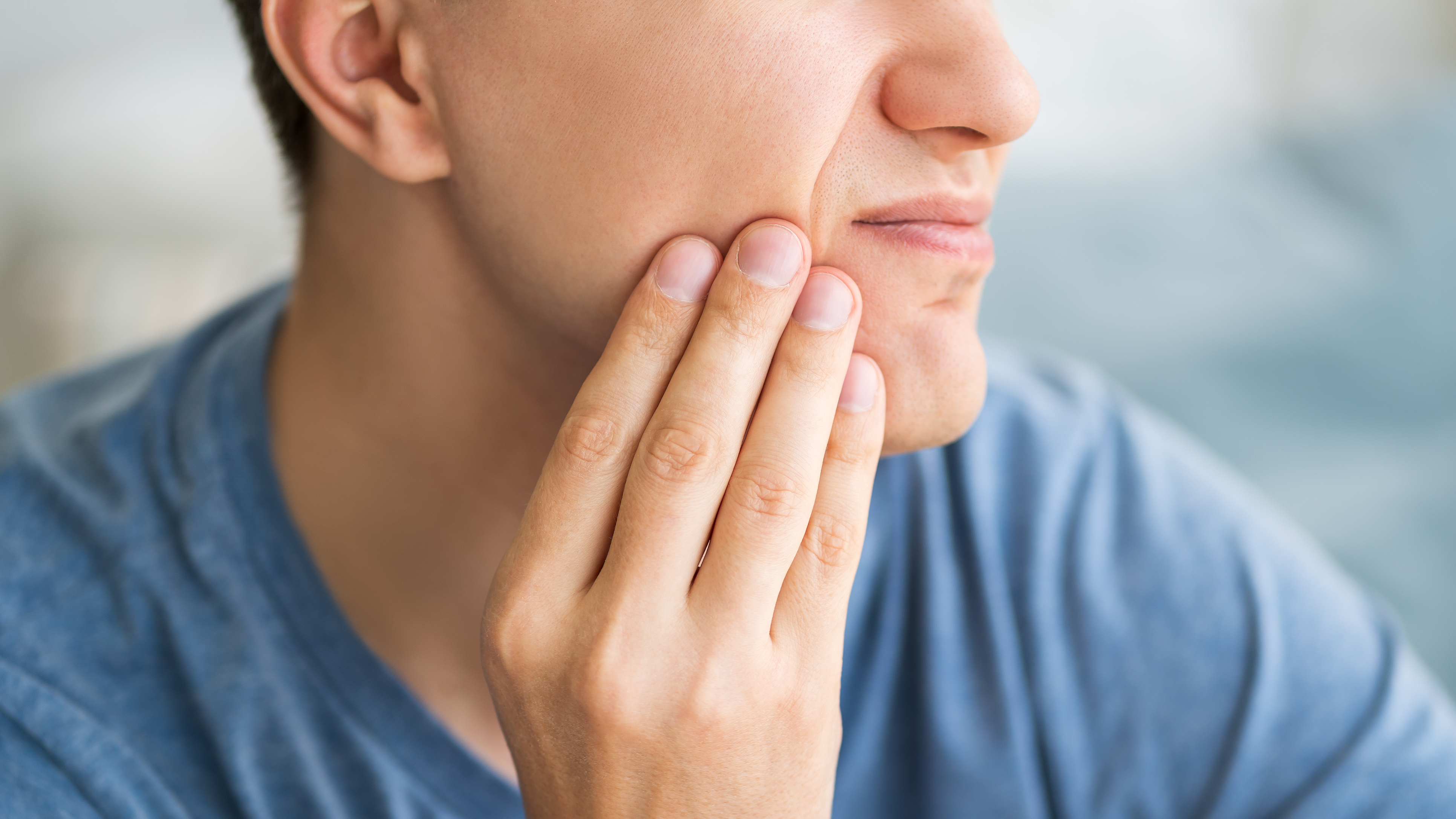 A male with his hand on his cheek having tooth pain
