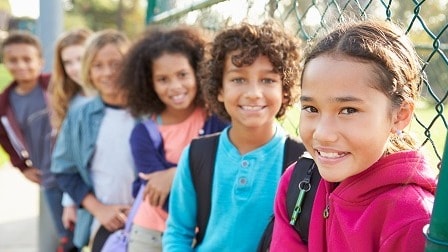School-aged children lean against a fence and smile together.