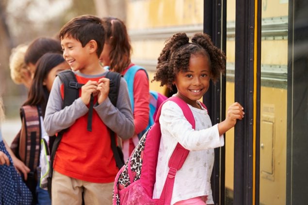 Smiling children walking onto a school bus