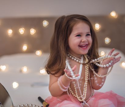 A two and a half year old girl tries on her mother's pearls.