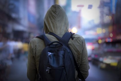 A view of the back of person wearing a backpack and a hooded sweatshirt outside in a cold busy urban setting