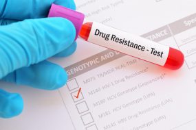 The form shows a test ordered for HIV-1 Drug Resistance. A gloved hand holds a blood sample collection vial with a “drug resistance test” label.