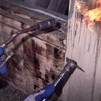 This 1999 photograph shows a worker using flames from a torch to assist in the removal of paint, demonstrating an exterior renovation method typically used on residences where lead-based paint was present. This method was found to contaminate nearby areas with lead.