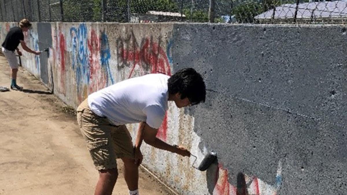 Photo of two teen Youth Advisory Board members cleaning up and painting the walls at the skate park with rollers. Photo credit: Upriver Youth Leadership Council
