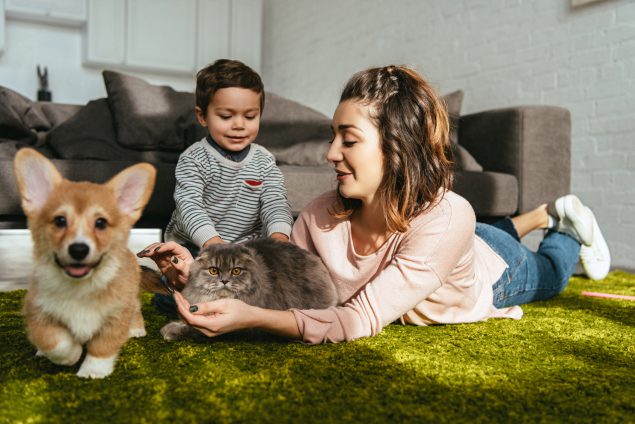 woman and little boy laying on floor with dog and cat in living room at home