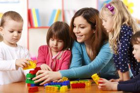 Nursery teacher and preschoolers playing with building blocks