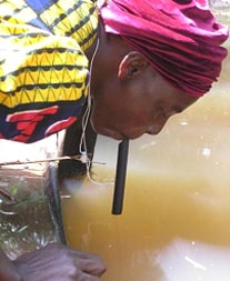 Nigerian woman drinking water directly from a pond through a pipe filter. Photo credit:  Emily Staub, 2002, The Carter Center.