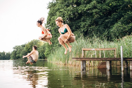 Three young adults jump into lake