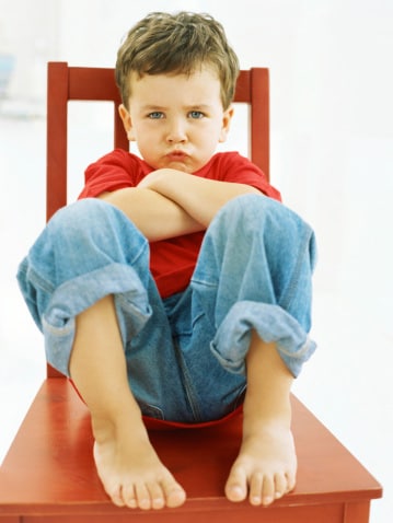 Boy sitting in timeout chair pouting