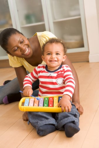 Mom wathcing toddler playing a toy xylophone
