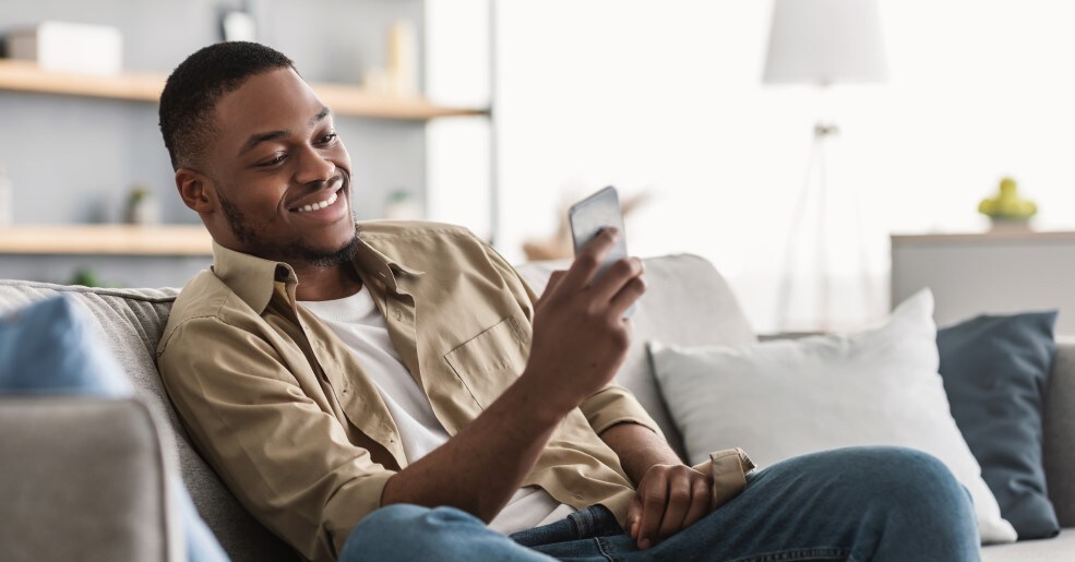 Man sitting on couch in living room smiling and using cell phone.