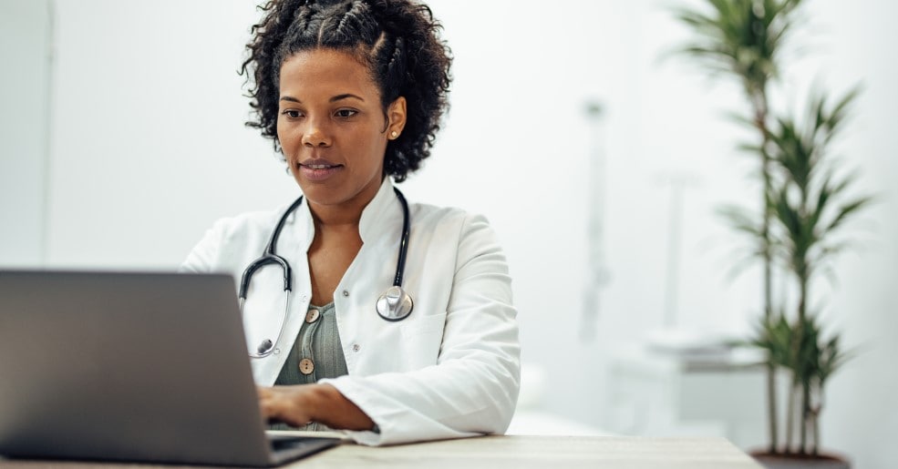 African American Doctor Sitting At Desk Using Laptop In Office