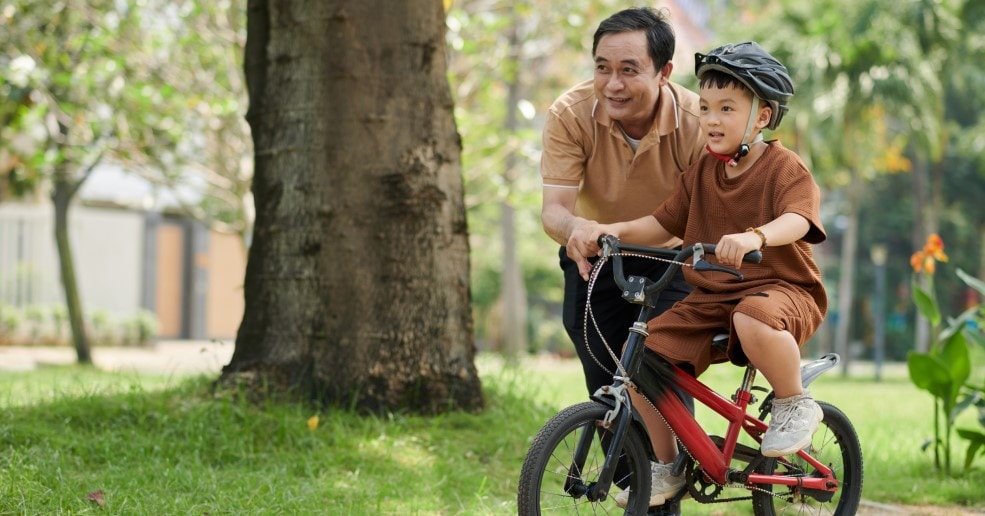 Father riding bike with young son in park.