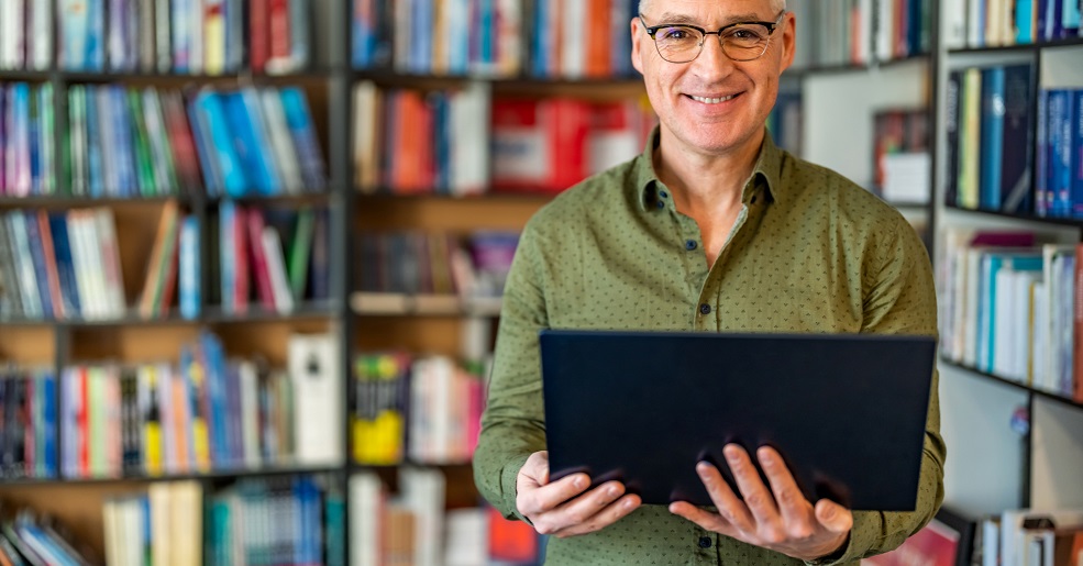 Author smiling. Standing in a library.