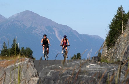 Two people on bicycles ride through mountainous area.