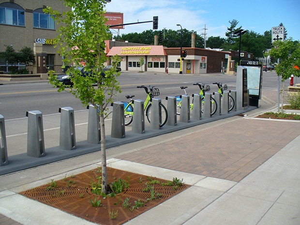 Bike share kiosks, some with bicycles, near a street