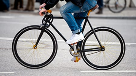 A cyclist wearing jeans and sneakers riding a bicycle