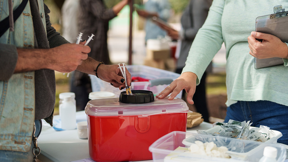 A man deposits used syringes into a red disposal container.