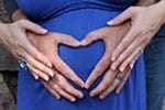 Foto de una mujer embarazada con las manos en su estómago formando un corazón.