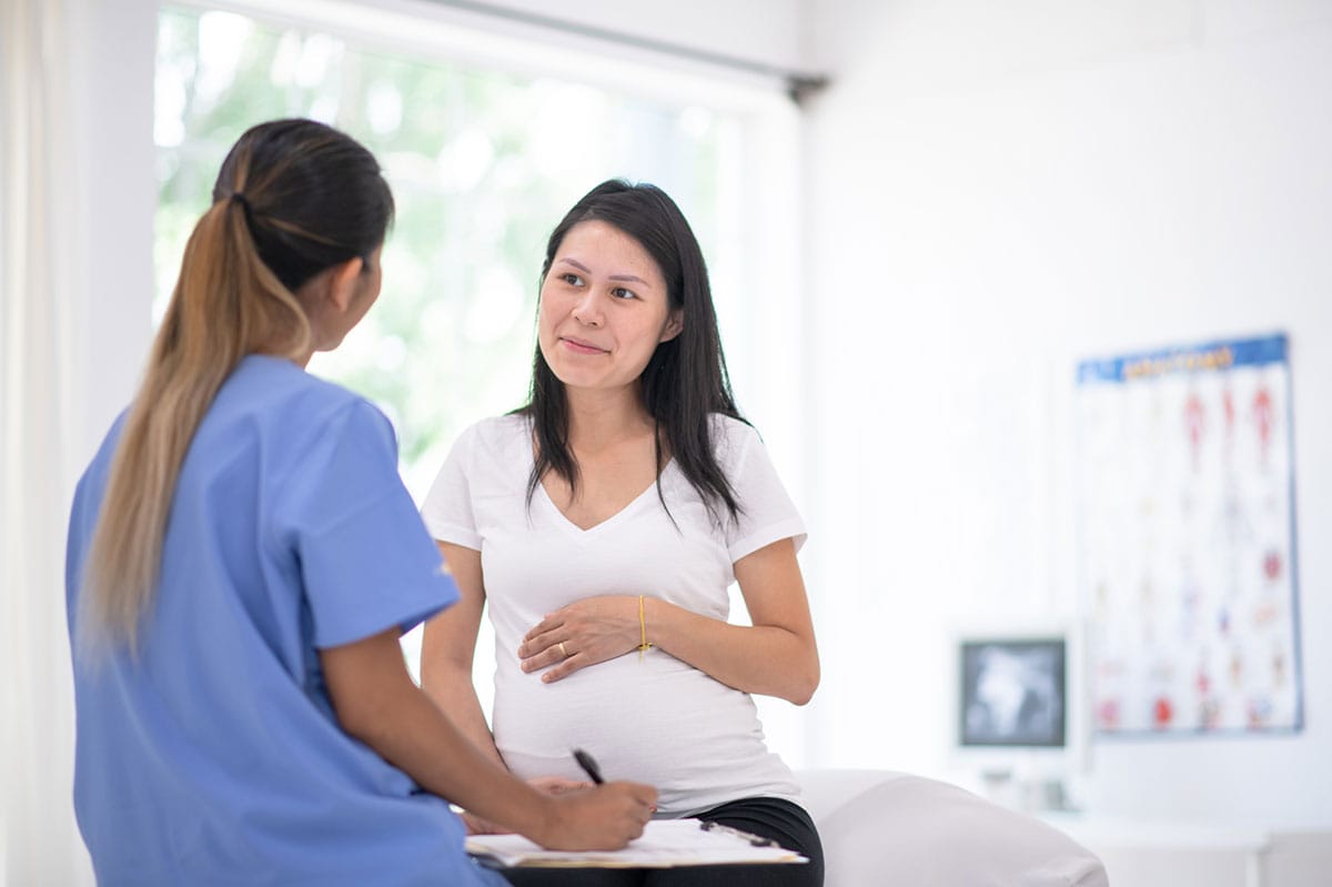 A pregnant woman smiles as she talks to her nurse in the doctor's office.