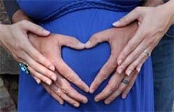 Las manos de un hombre y una mujer sobre el estómago de la mujer embarazada, formando un corazón