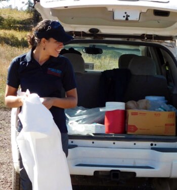 Helena Archer preparing supplies near a vehicle's hatchback