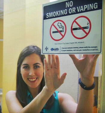 Photo of Allison Napier posting a sign to a window that reads No Smoking or Vaping