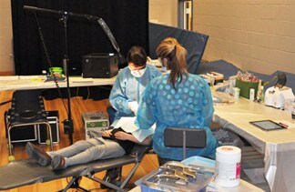 This picture shows a school-based dental clinic with a child being treated by two dental professionals.