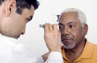 The photo shows an older, African American man getting his eyes examined by a doctor.