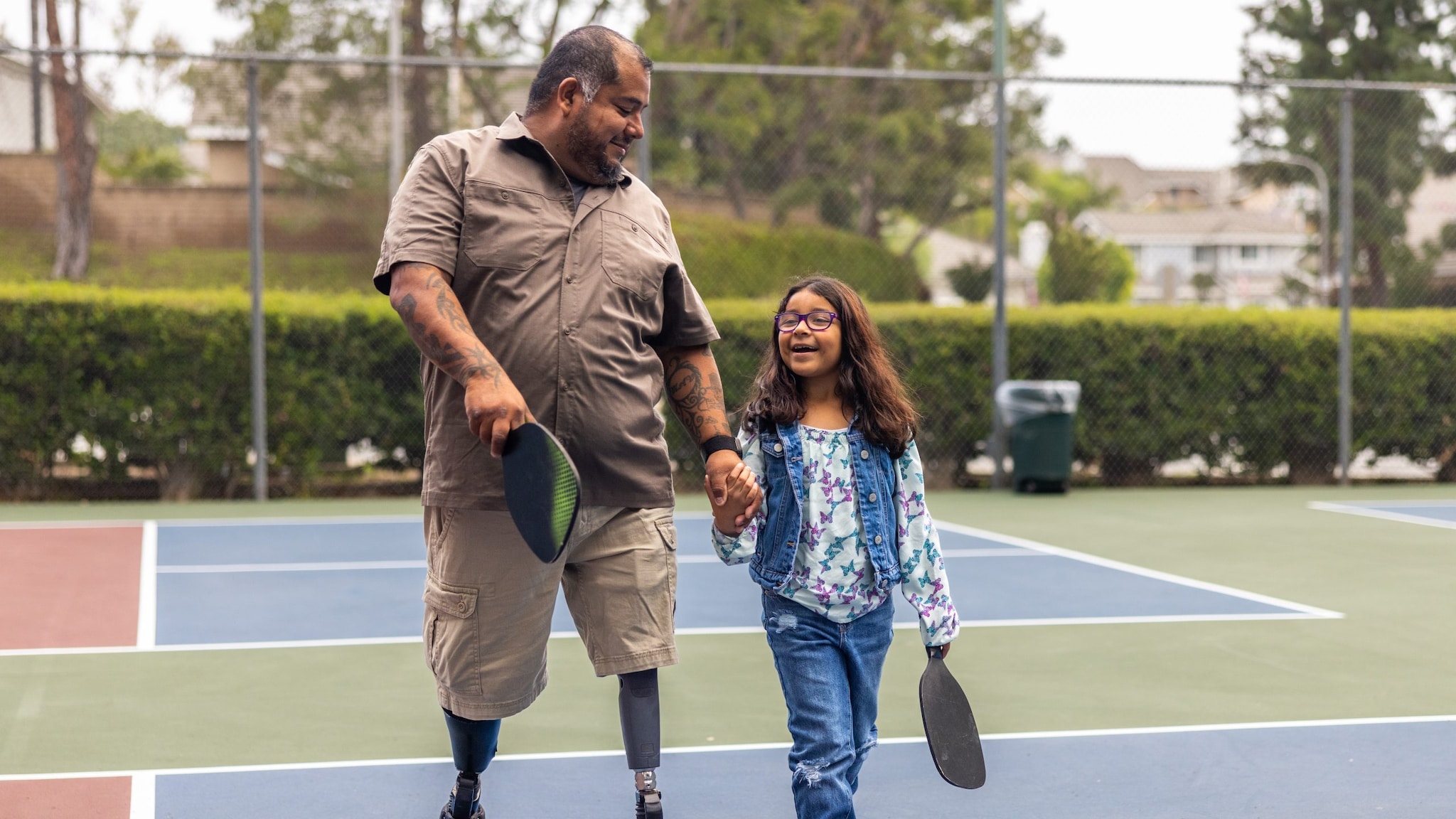 Father with prosthetic legs and daughter on pickleball court.