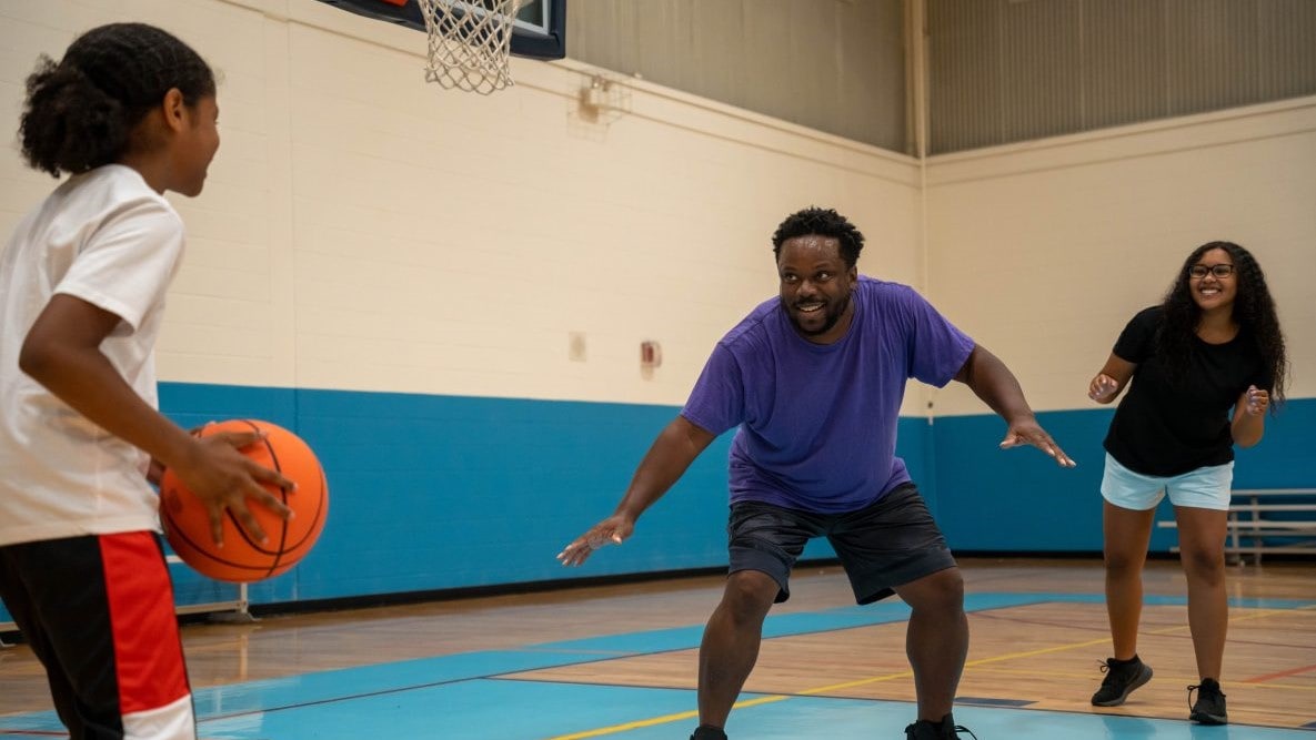 Father inside a gym playing basketball with two children.